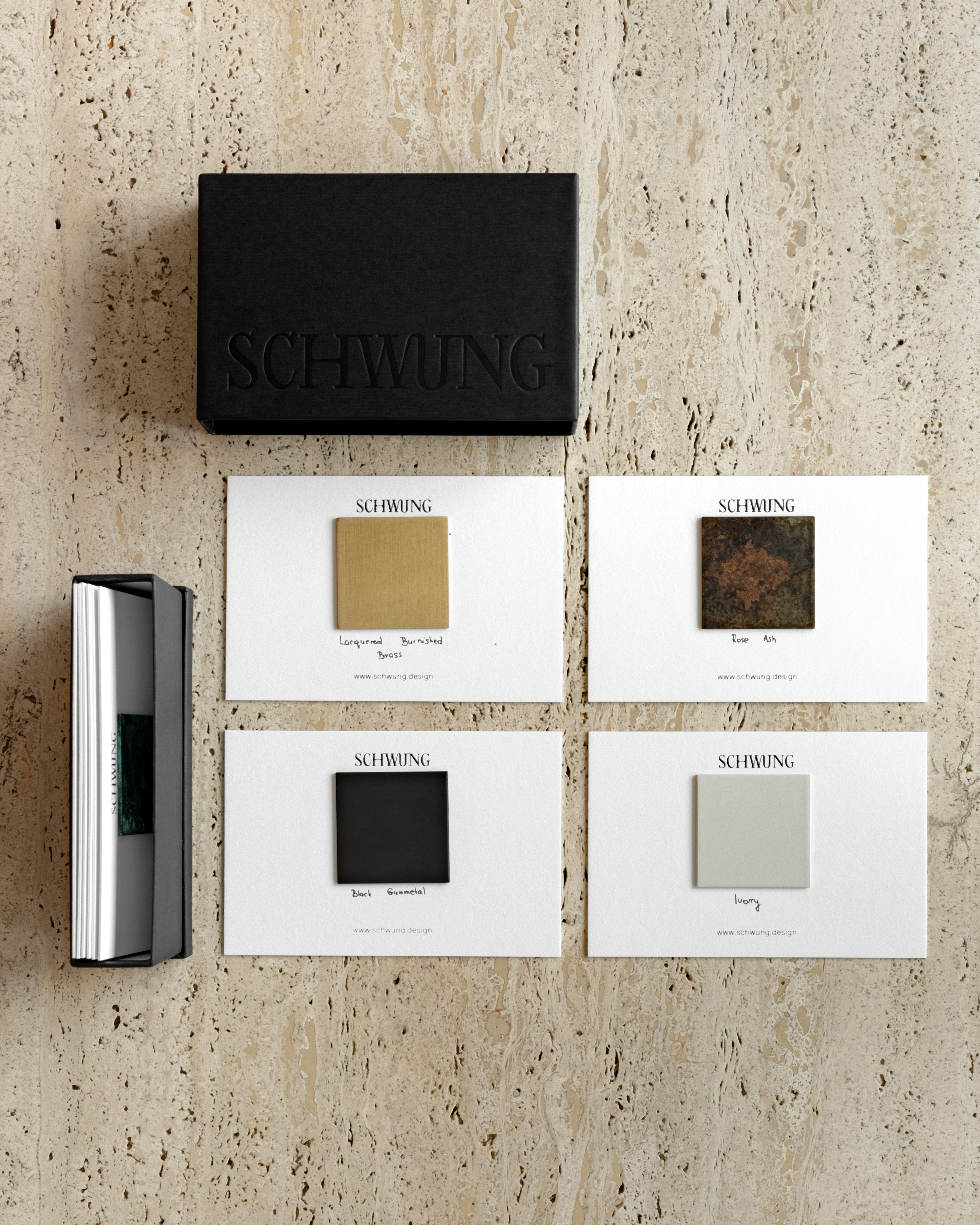 Schwung Small Finish Sample Box with 10 brass finish sample cards on travertine surface.