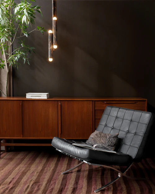 Vesta pendant in rose ash finish, suspended above a refined interior with wooden sideboard and leather lounge chair by Schwung