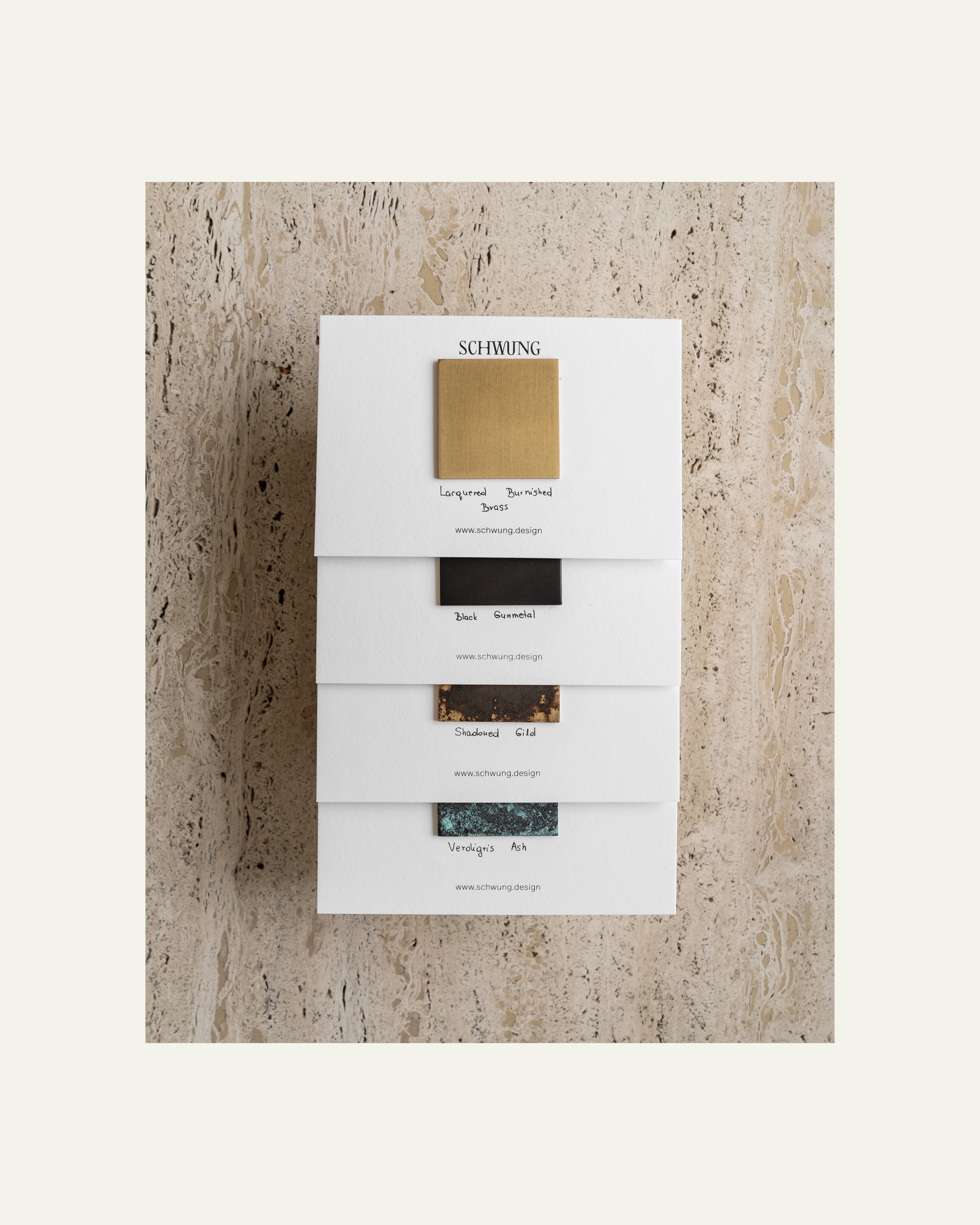 Schwung Small Finish Sample Box with 10 brass finish sample cards on travertine surface.