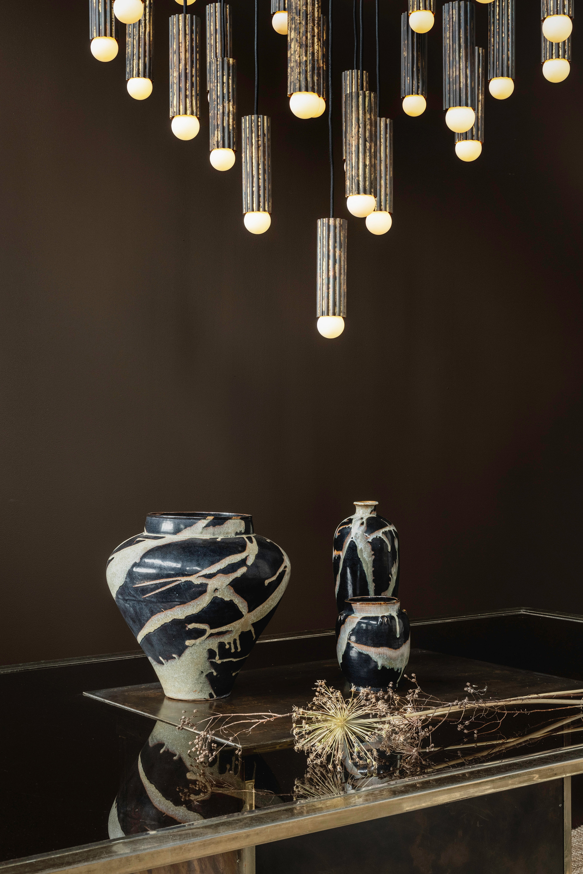 Vesta brass and glass chandelier above a reflective console with decorative ceramic vases in a moody luxury interior by Schwung.