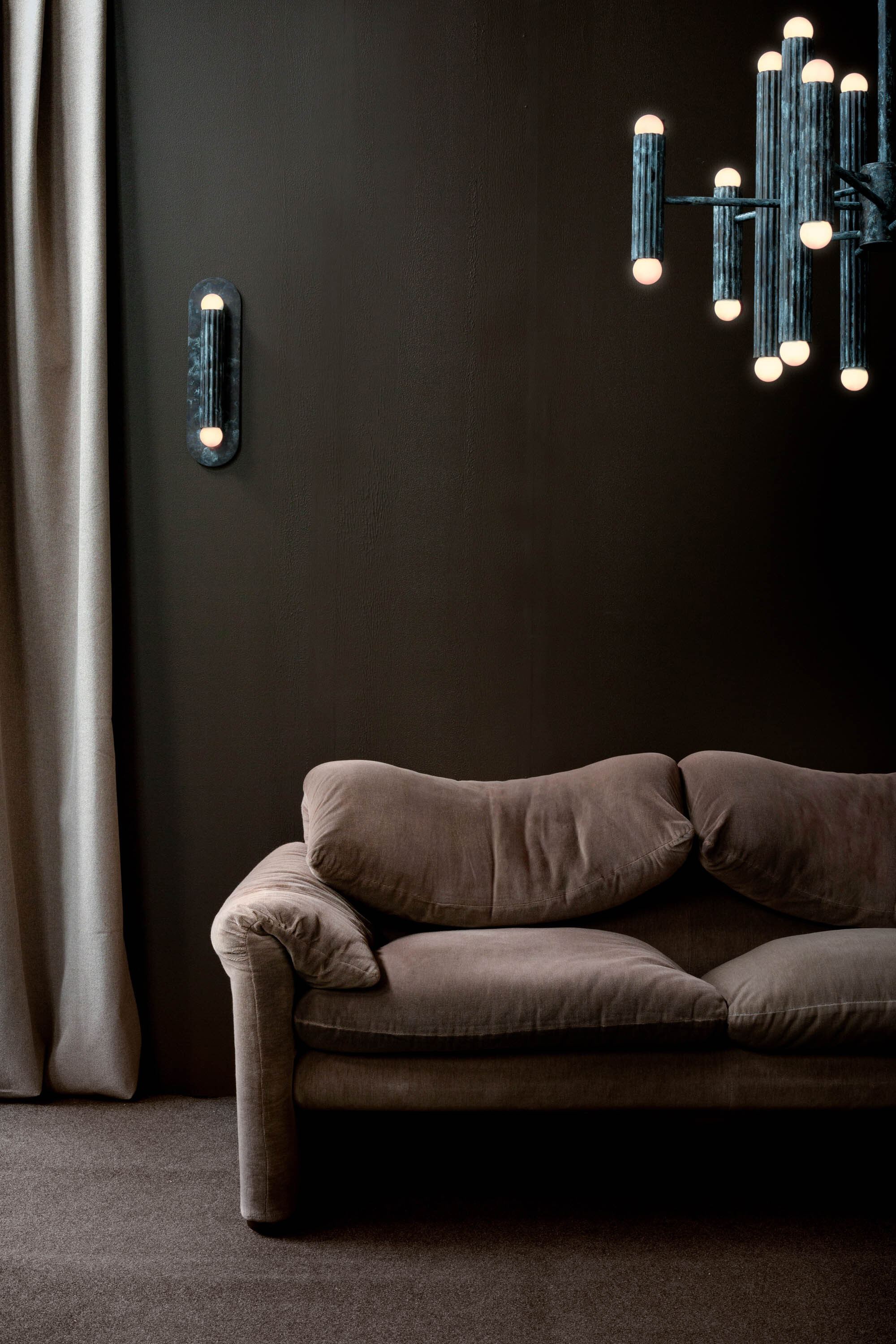 Moody luxury living room with brown velvet sofa, dark walls and illuminated Schwung glass pendant lights.
